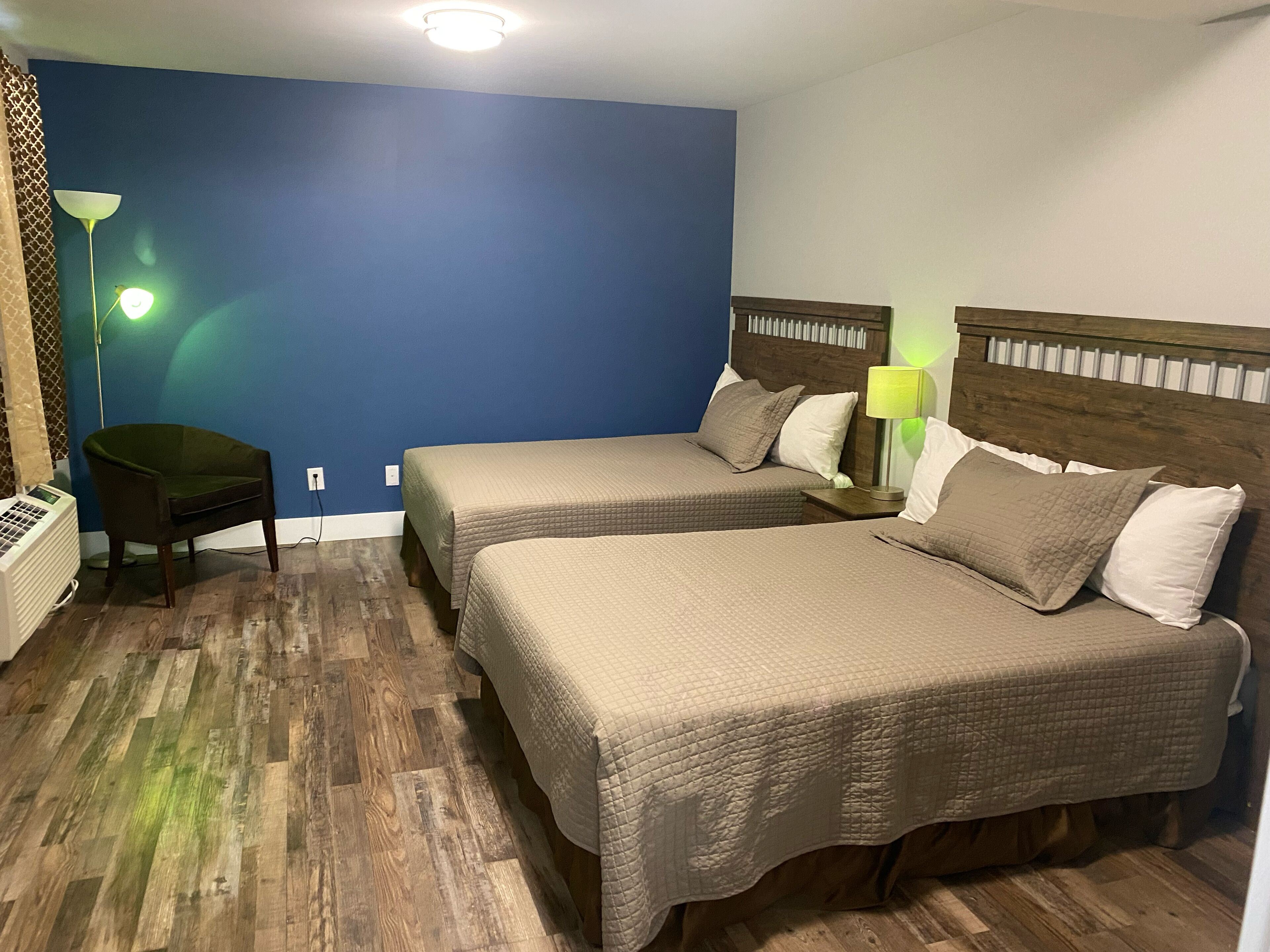 A hotel room with two beds, a chair, a lamp, and a heater.