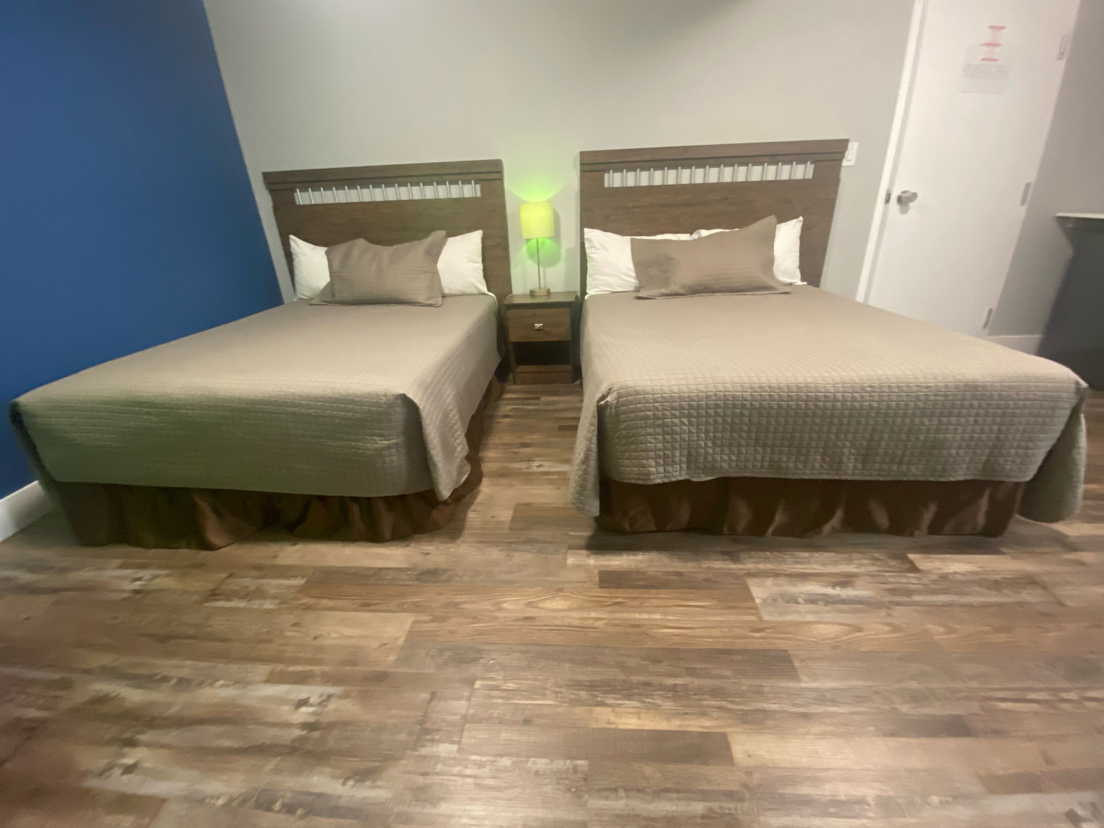 Two single beds with wooden headboards, a nightstand between them, and a wooden floor.