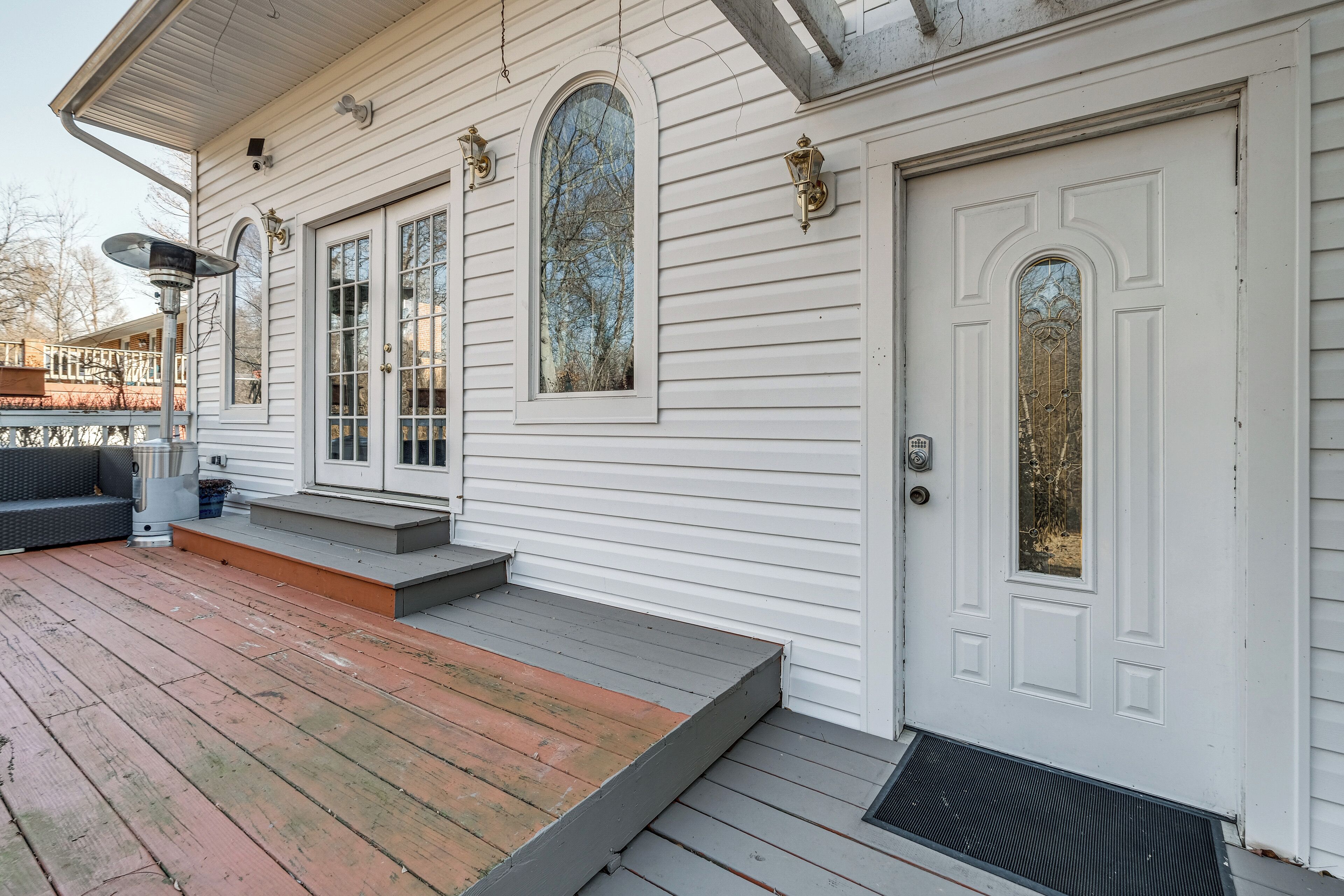 A white house with a front porch, a door with a glass panel, and a window with a view of trees.