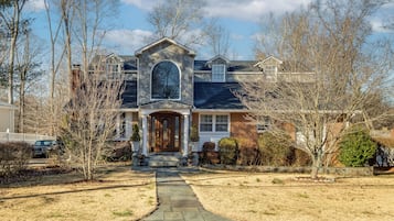 A two-story house with a stone entrance, a front porch, and a driveway leading to a parked car.