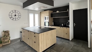 Een moderne keuken met een centraal eiland, inbouwapparatuur en een zwarte deur.