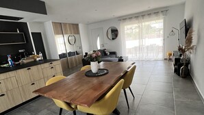 Een moderne keuken met een eethoek, met een houten tafel en gele stoelen, een inbouwoven en een groot raam.