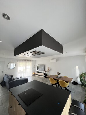 Een moderne woonruimte met een centraal eiland, een eethoek met gele stoelen en een groot raam dat zorgt voor natuurlijk licht.