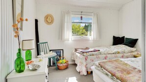 Un dormitorio con dos camas, una ventana que da a zonas verdes, un aparador y una silla.