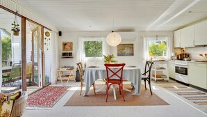 Un luminoso y espacioso salón-comedor con un gran ventanal, una mesa de comedor preparada para dos personas y una zona de cocina con armarios y electrodomésticos blancos.