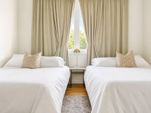 Ein Hotelzimmer mit zwei Betten, einem Nachttisch, einer Lampe und einem Fenster mit Vorhängen.