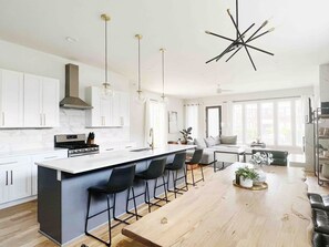 A modern kitchen with white cabinets, a central island with bar stools, pendant lighting, and a unique ceiling light fixture. - Skyline View - Walk to Broadway (Nashville)