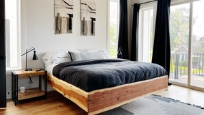 A modern bedroom with a wooden bed frame, a bedside table with a lamp, and a view of the outdoors through large windows. - New! Downtown, Rooftop, Walkable to The Gulch, Music Row & 1M to Broadway! (Nashville)