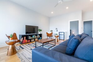 Ein modernes Wohnzimmer mit einer großen Couch, einem Couchtisch, einem Fernseher und einem Bücherregal.