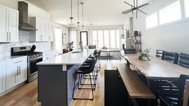 A modern kitchen with white cabinets, a large island, and a dining area with a long wooden table and black chairs. - New! Downtown, Rooftop, Walkable to The Gulch, Music Row & 1M to Broadway! (Nashville)