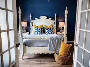 Een slaapkamer met een wit hemelbed, twee bedlampen en een geweven mand met een geel kussen.