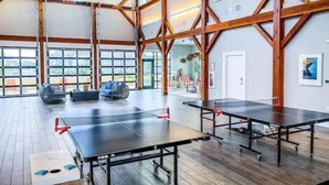A spacious room with ping pong tables, wooden beams, large windows, and a view of the outdoors. - A Block from the Dock in Beau Coast Classic (Beaufort)
