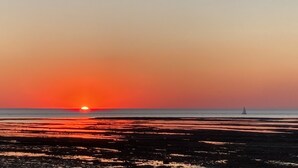 A sunset over a beach with a sailboat in the distance.