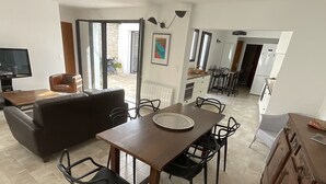 A modern living room with a brown sofa, a wooden dining table with chairs, and a TV.