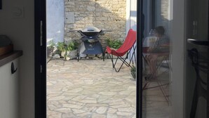 A stone patio with a grill, a red chair, and a person sitting at a table.