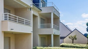 Un edificio residencial de varios pisos con balcones, techo plano y un pequeño árbol en primer plano.
