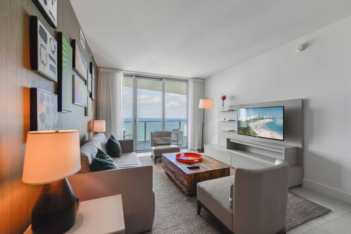 Une chambre d’hôtel moderne dotée d’une grande télévision, de sièges confortables, d’une vue sur la mer et d’un balcon.