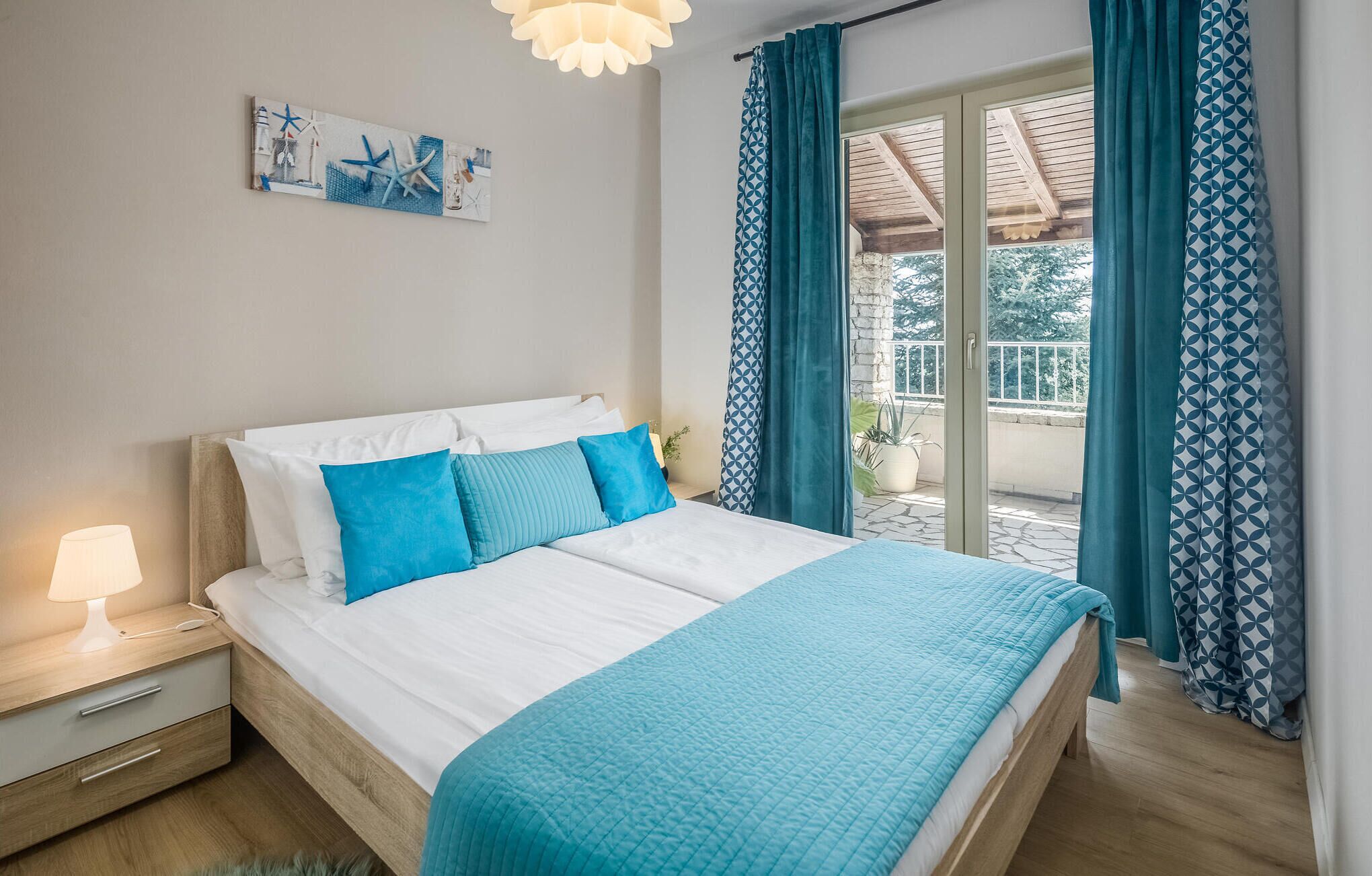 Un dormitorio con cama, mesita de noche, lámpara, ventana con cortinas y una obra de arte en la pared.
