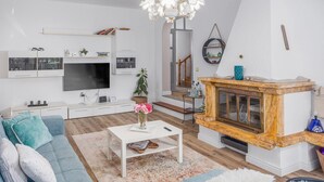 Moderni olohuone, jossa on litteänäyttöinen televisio, valkoiset huonekalut, maljakkoon asetettu kahvipöytä ja portaat, jotka johtavat ylempään kerrokseen.