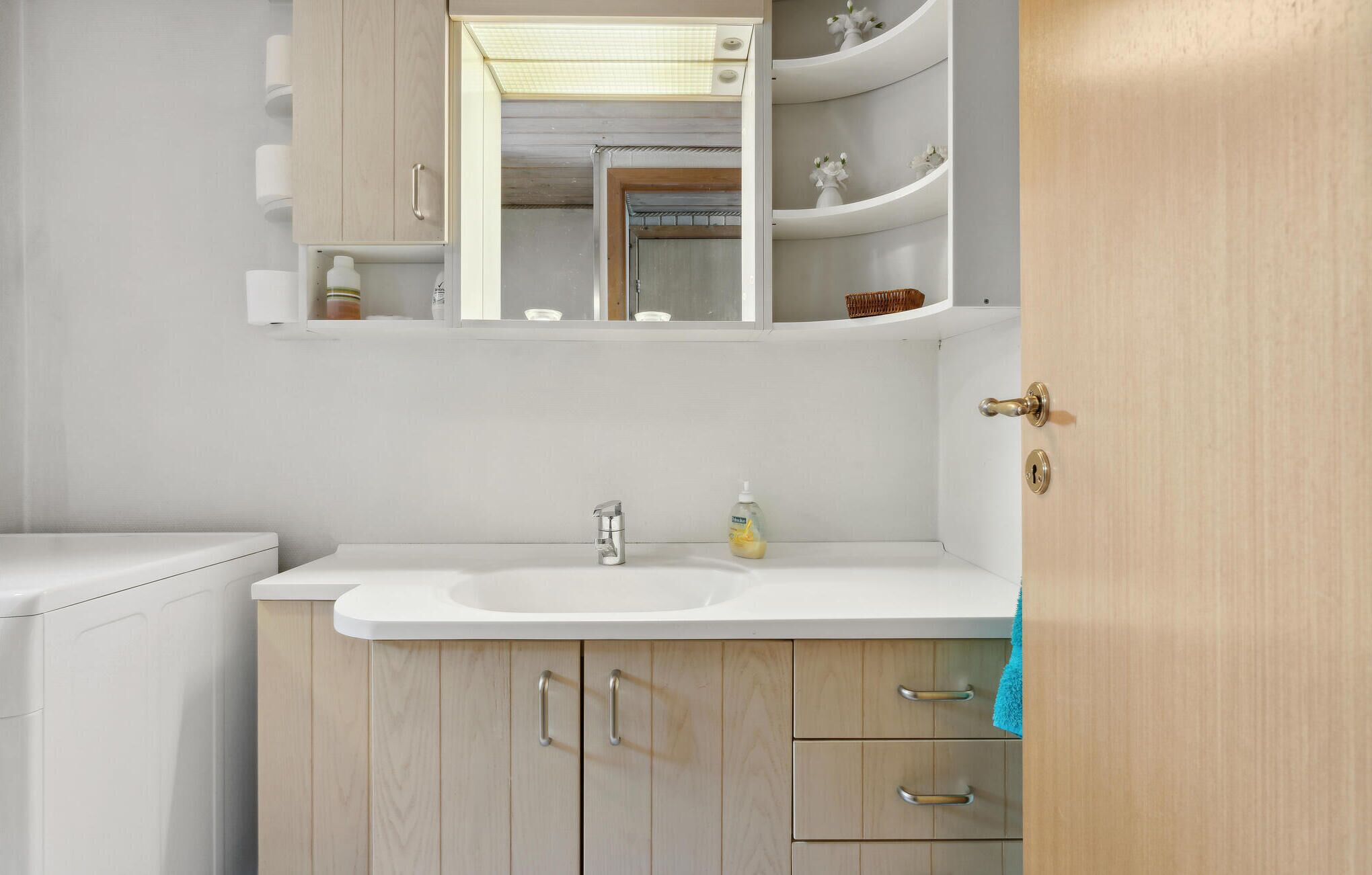 A bathroom with a white sink, wooden cabinets, a mirror, and a towel hanging on the door.
