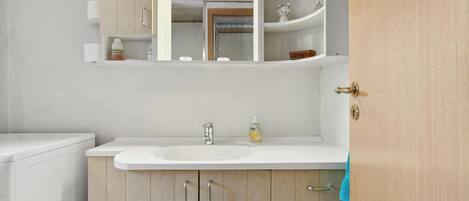 A bathroom with a white sink, wooden cabinets, a mirror, and a towel hanging on the door.