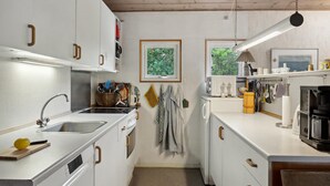 Een compacte keuken met witte kastjes, een roestvrijstalen spoelbak, een magnetron en een koffiezetapparaat. Er zijn twee ramen die natuurlijk licht binnenlaten, en een hanglamp boven het aanrecht.