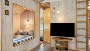 Een knus ingerichte kamer met houten details, een grote flatscreen televisie, een houten tv-meubel en een raam met uitzicht op groen.