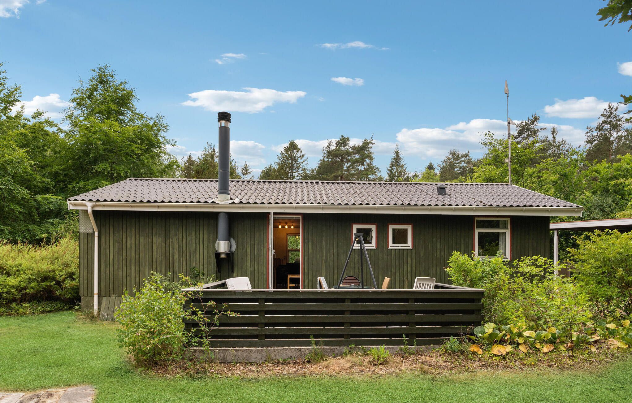 A rustic cabin with a chimney, a small porch with chairs, and a door leading to an interior room.
