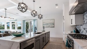 A modern kitchen with a large island, dark cabinets, a gas stove, and pendant lighting. - Sizzling Summer Rates at Surf Side Beach House  GULF VIEWS Elevator (Beach Retreats) (Holmes Beach)