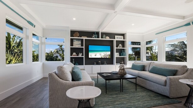 A modern living room with a large TV, two sofas, a coffee table, and a bookshelf. - Sizzling Summer Rates at Surf Side Beach House  GULF VIEWS Elevator (Beach Retreats) (Holmes Beach)