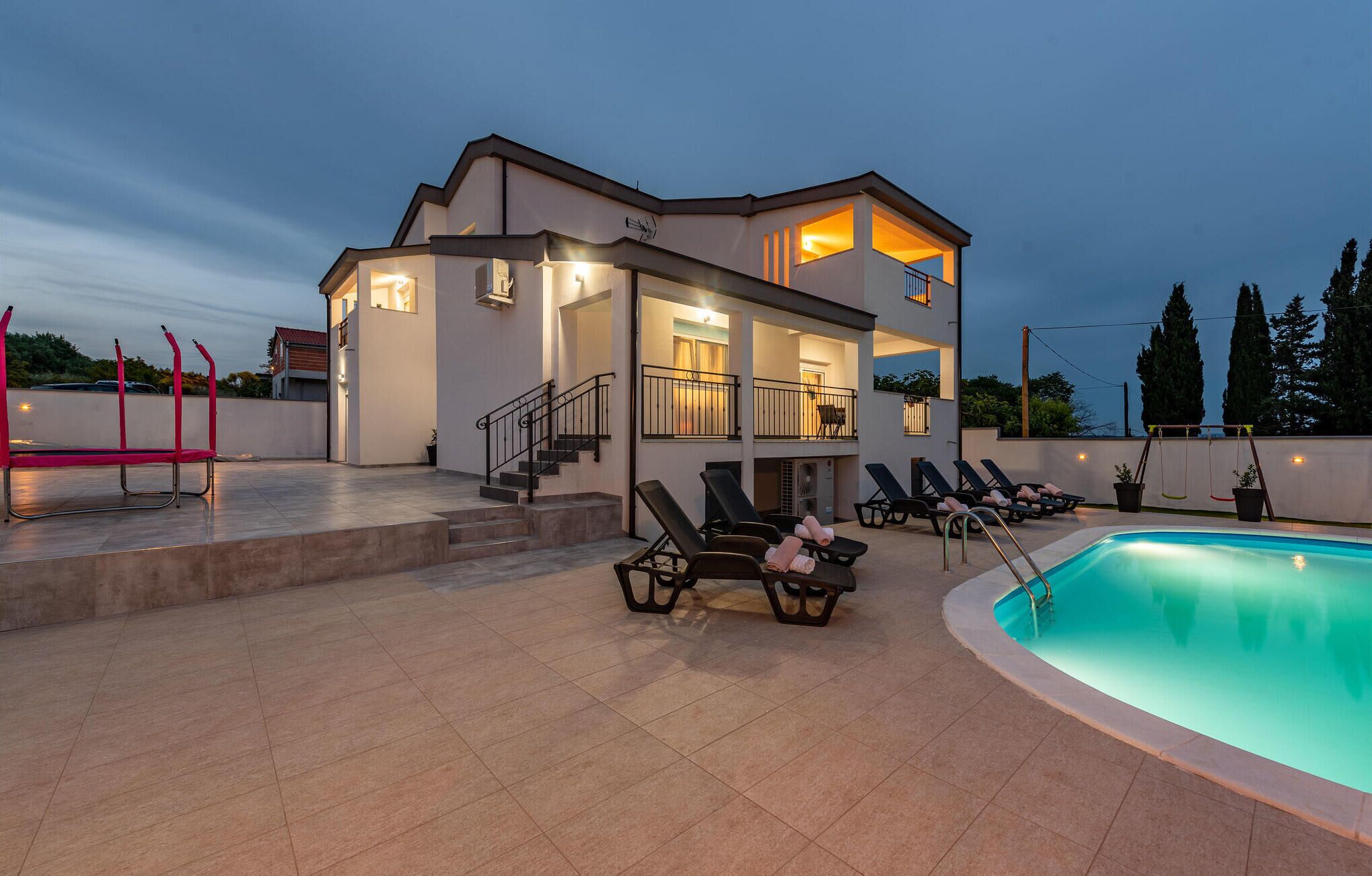 Un edificio moderno de dos pisos con piscina, mobiliario exterior y una escalera que conduce al piso superior.