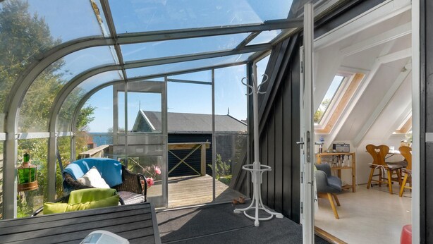 A modern, open-plan living space with a glass enclosure, a dining area with wooden furniture, and a view of the outdoors. - Beautiful home in Allinge with WiFi (Allinge)