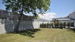 Une cour clôturée avec de l’herbe, un arbre et un bâtiment doté d’un toit plat.