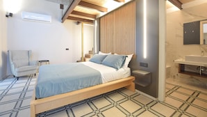 Une chambre à coucher moderne comprenant un lit, une chaise, une table de chevet et une salle de bain avec un lavabo et un miroir.