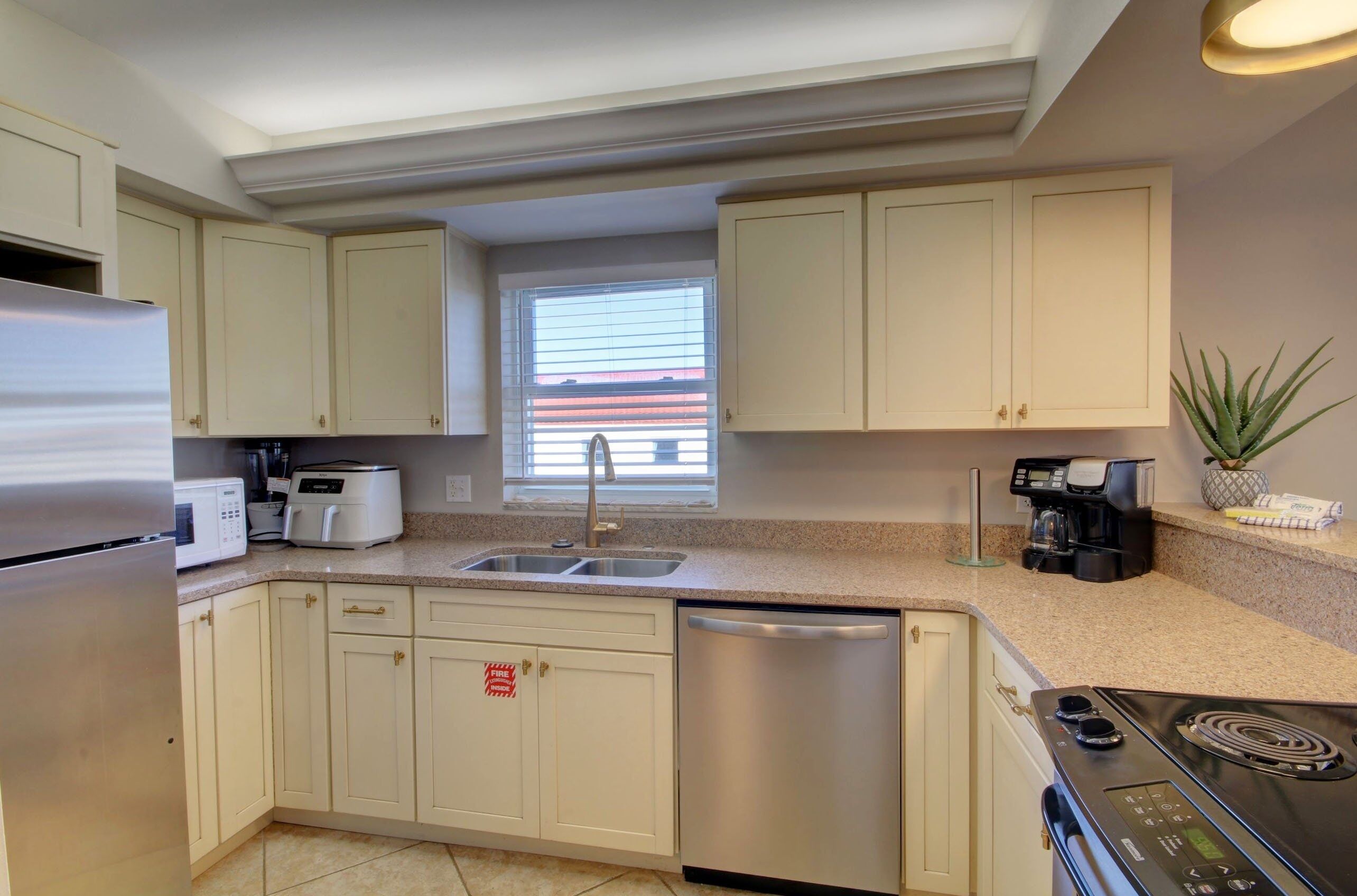 A modern kitchen with white cabinets, a stainless steel refrigerator, a dishwasher, a stove, and a coffee maker.