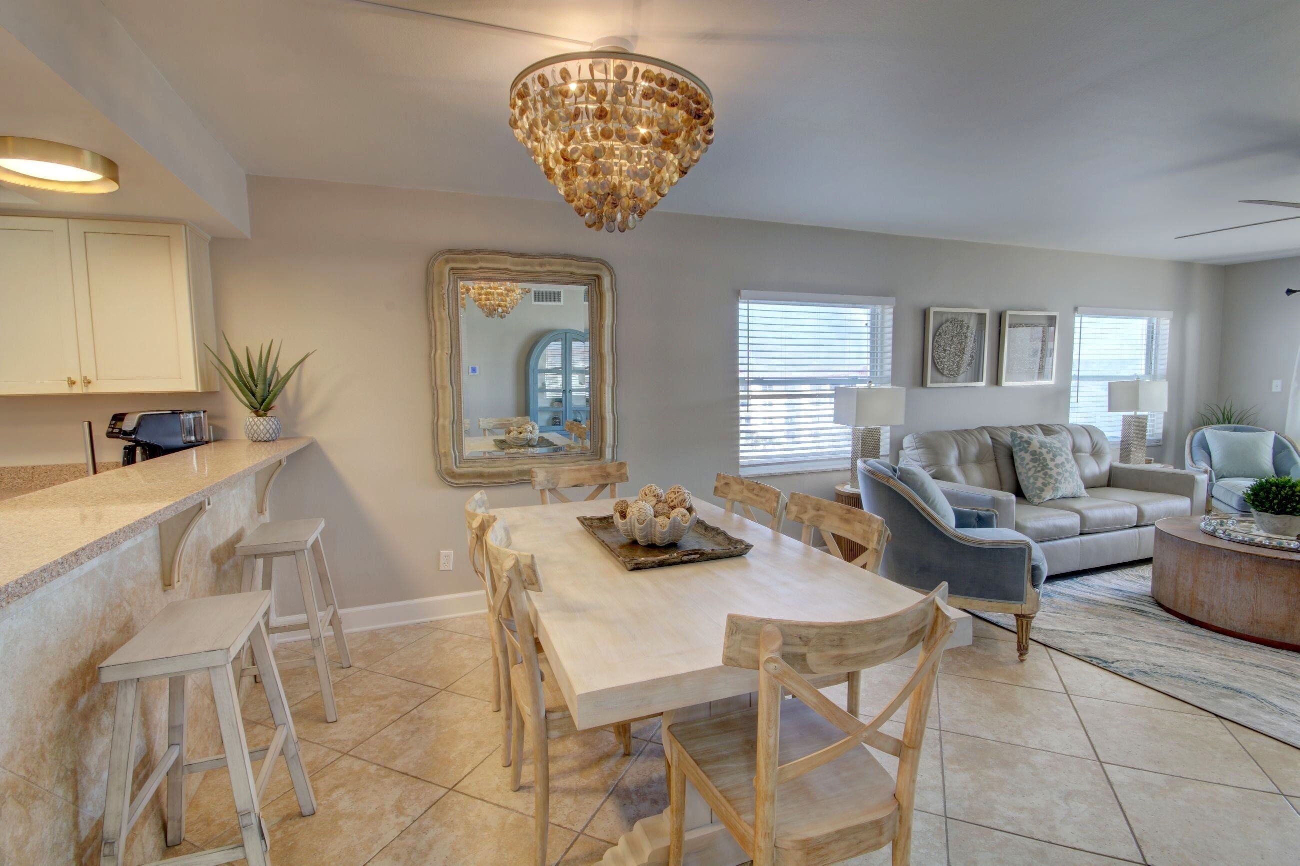 A spacious living room with a large chandelier, a dining area with a white table and wooden chairs, and a light-colored sofa.