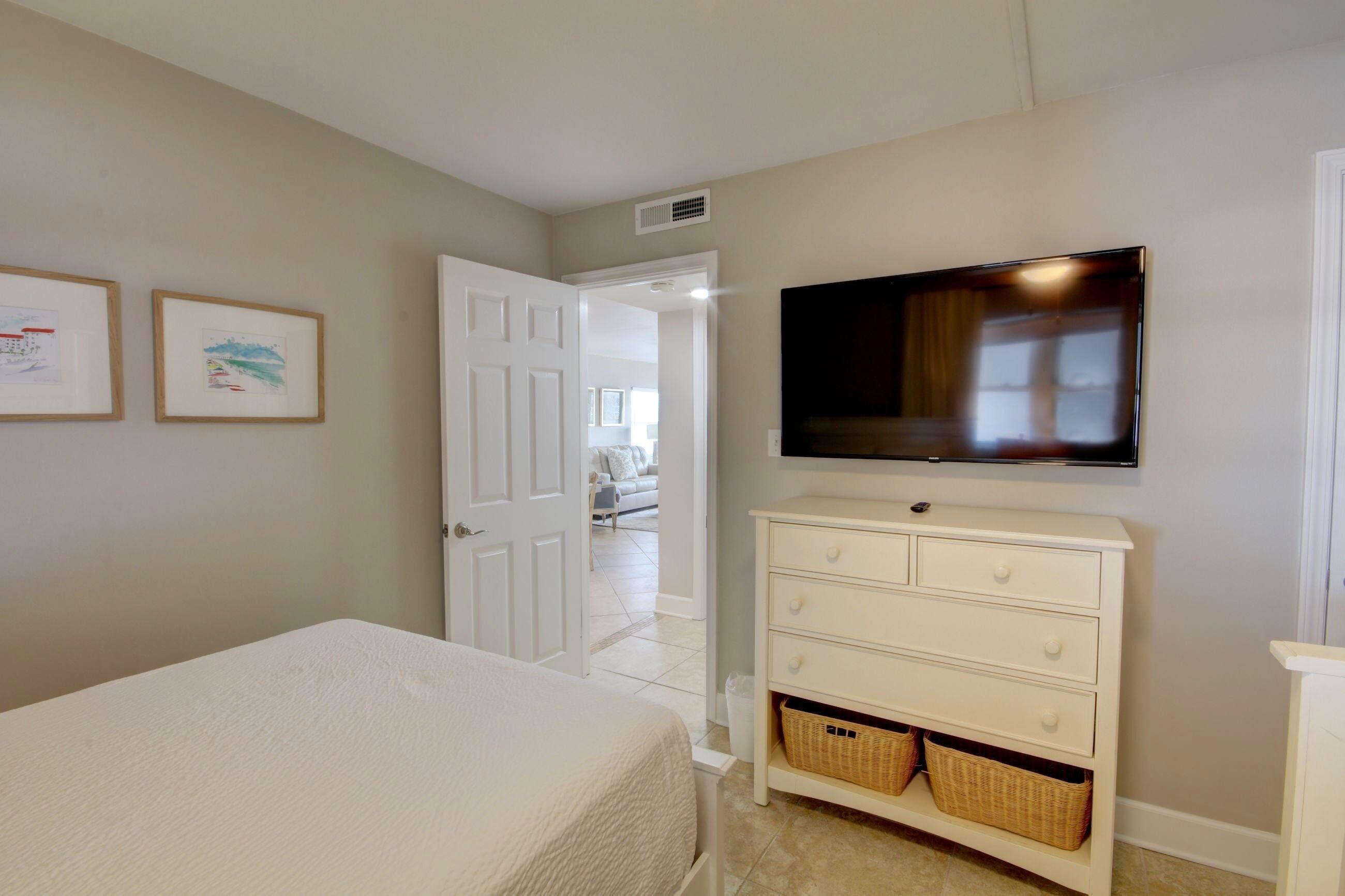 A bedroom with a bed, a dresser, a television, and framed pictures on the wall.