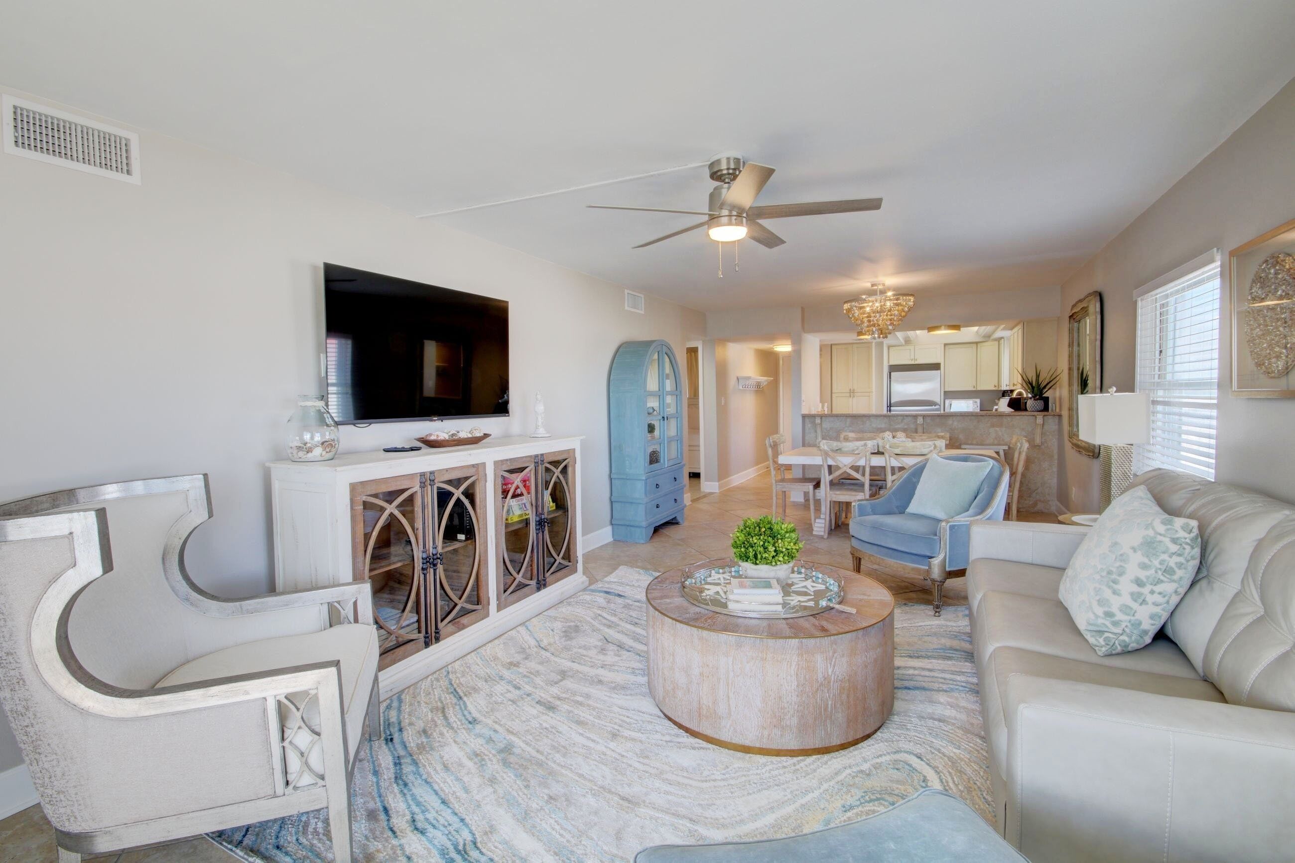 A modern living room with a flat-screen TV, a ceiling fan, and a dining area with a chandelier.