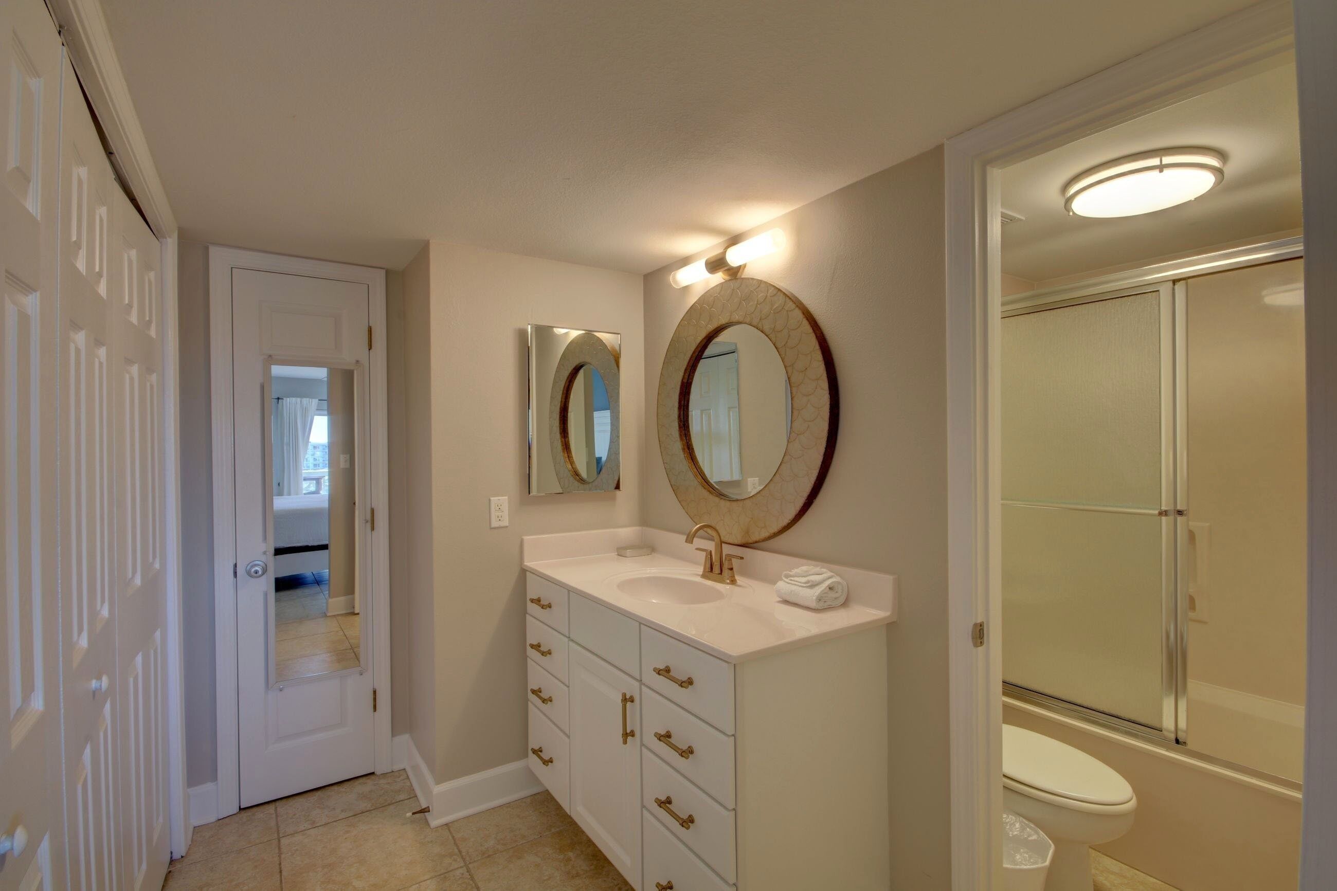 A bathroom with a white vanity, two mirrors, a sink, and a shower.