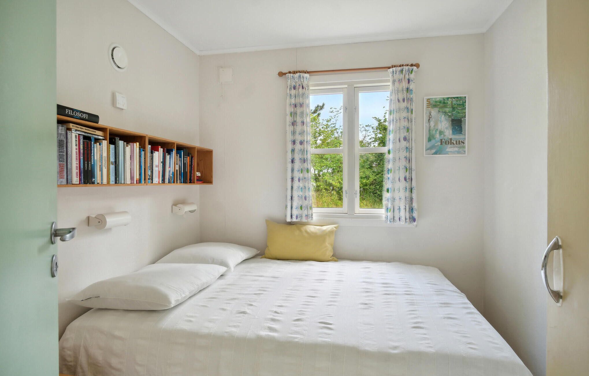 Een slaapkamer met een bed, een boekenkast, een raam met gordijnen en een wandlamp.