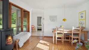 Ein gemütliches Zimmer mit Kaminofen, einem Esstisch mit Stühlen und Blick ins Grüne.