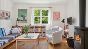 Ein gemütliches Wohnzimmer mit einer Couch, einem gestreiften Sessel, einem Couchtisch, einem Bücherregal, einem Kamin und einem Fernseher.