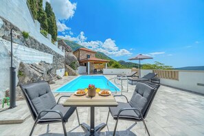 Un espace piscine aménagé sur le toit, avec un bâtiment en pierre, des sièges extérieurs et une vue sur les montagnes.