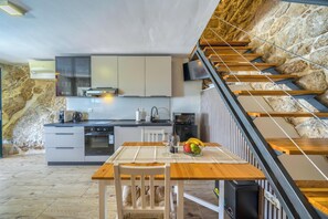 A modern kitchen with a dining area, a stone wall, and a wooden staircase. - Recently Built, Cosy Retreat for Two, A/C, Private Pool with Superb Views over the Konavle Valley! (Dubravka)