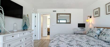 Un dormitorio con cama, cómoda, ventilador de techo, televisor y puerta que da a un baño.