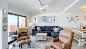 Un salon moderne comprenant un canapé, deux fauteuils, une table basse et un ventilateur de plafond.
