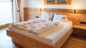 Una cama de madera con colcha y almohadas estampadas, una mesita de noche con lámpara y un cuadro en la pared.