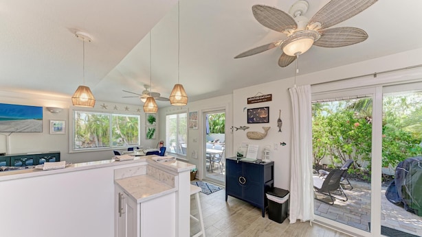 A modern kitchen with a central island, pendant lights, ceiling fans, and large windows offering views of the outdoors. - Salt Air East managed by Beach Retreats (Holmes Beach)
