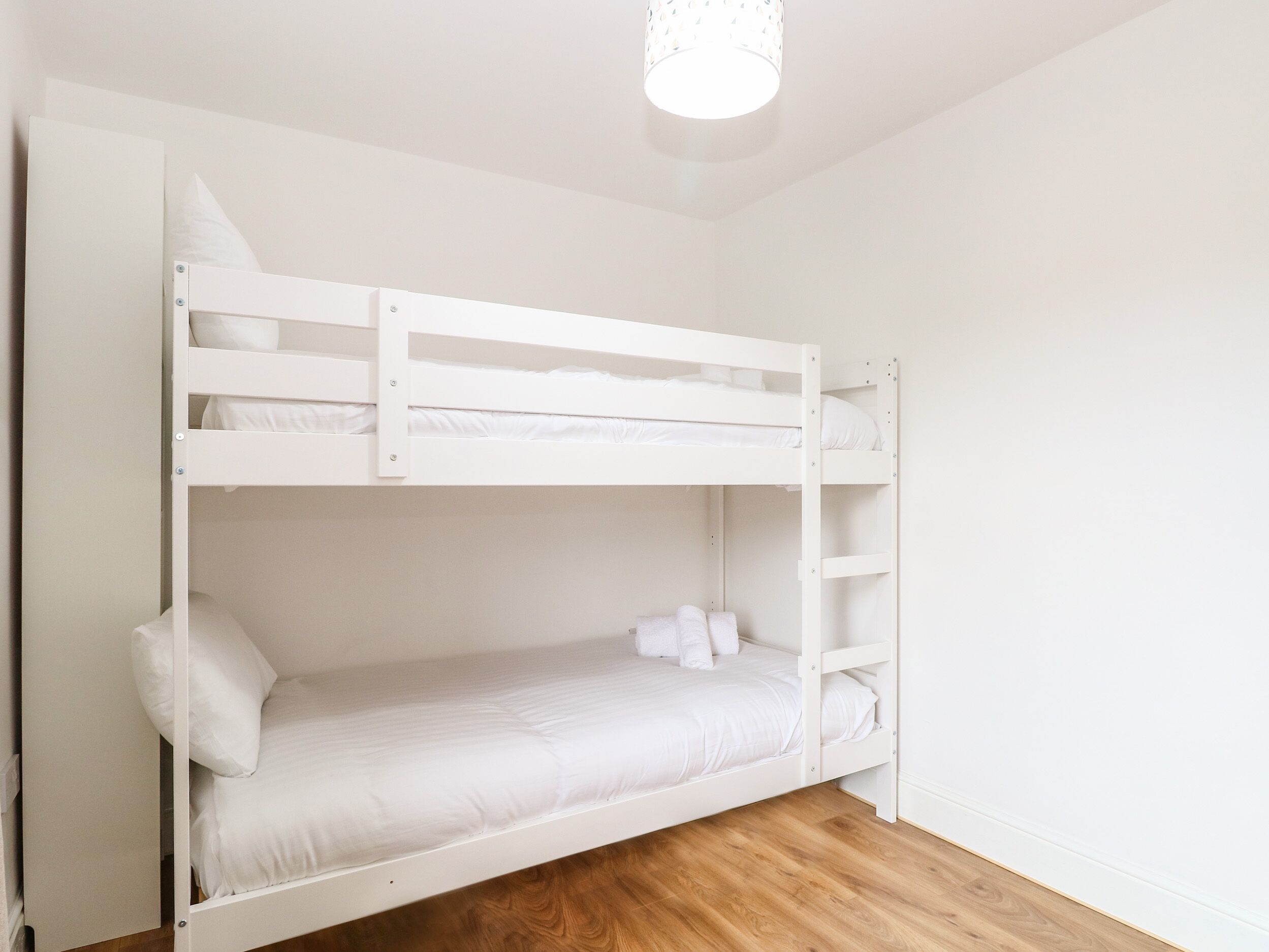 A bunk bed in a room with white walls and wooden flooring.