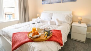 A neatly made bed with white linens, a tray with croissants, juice, and a coffee mug, and a painting above the bed. - Seaside House (Great Yarmouth)